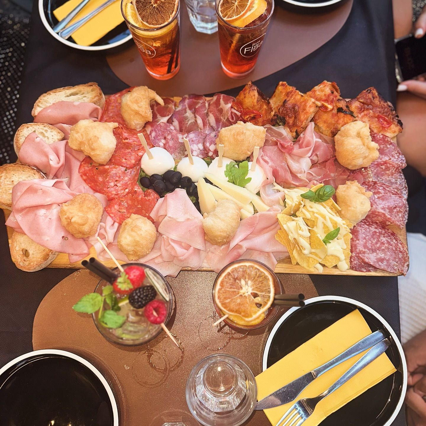 Tagliere di salumi, formaggi e pasta fritta, accompagnato da cocktail e apparecchiato al tavolo.