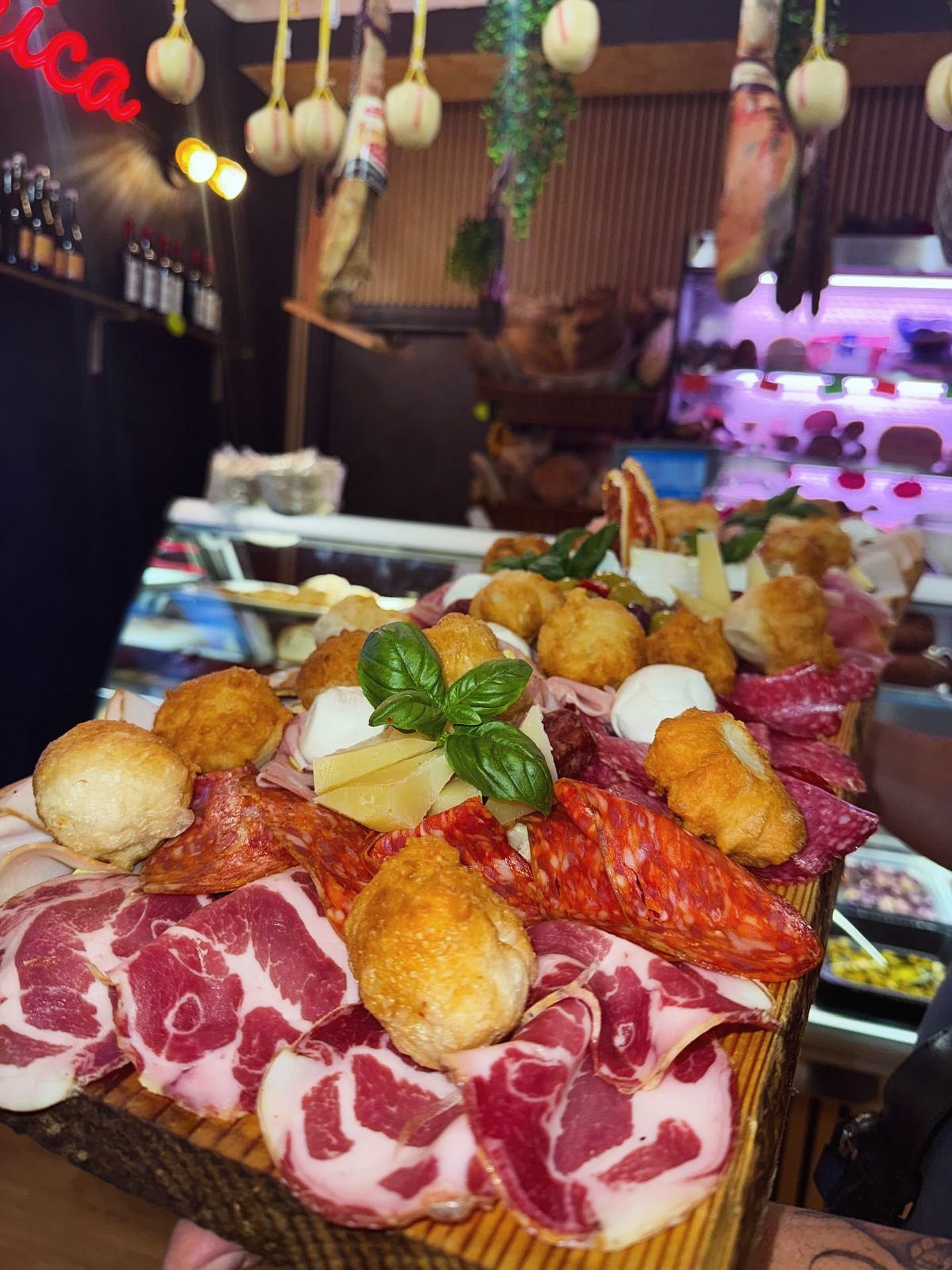 Tagliere di salumi con carni, formaggi e polpette fritte, in un ambiente da gastronomia.