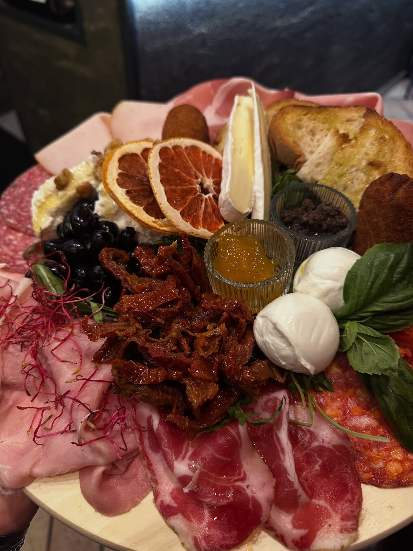 Tagliere di salumi con carni, formaggi, olive, pomodori secchi e pane, caratterizzato da colori vivaci.