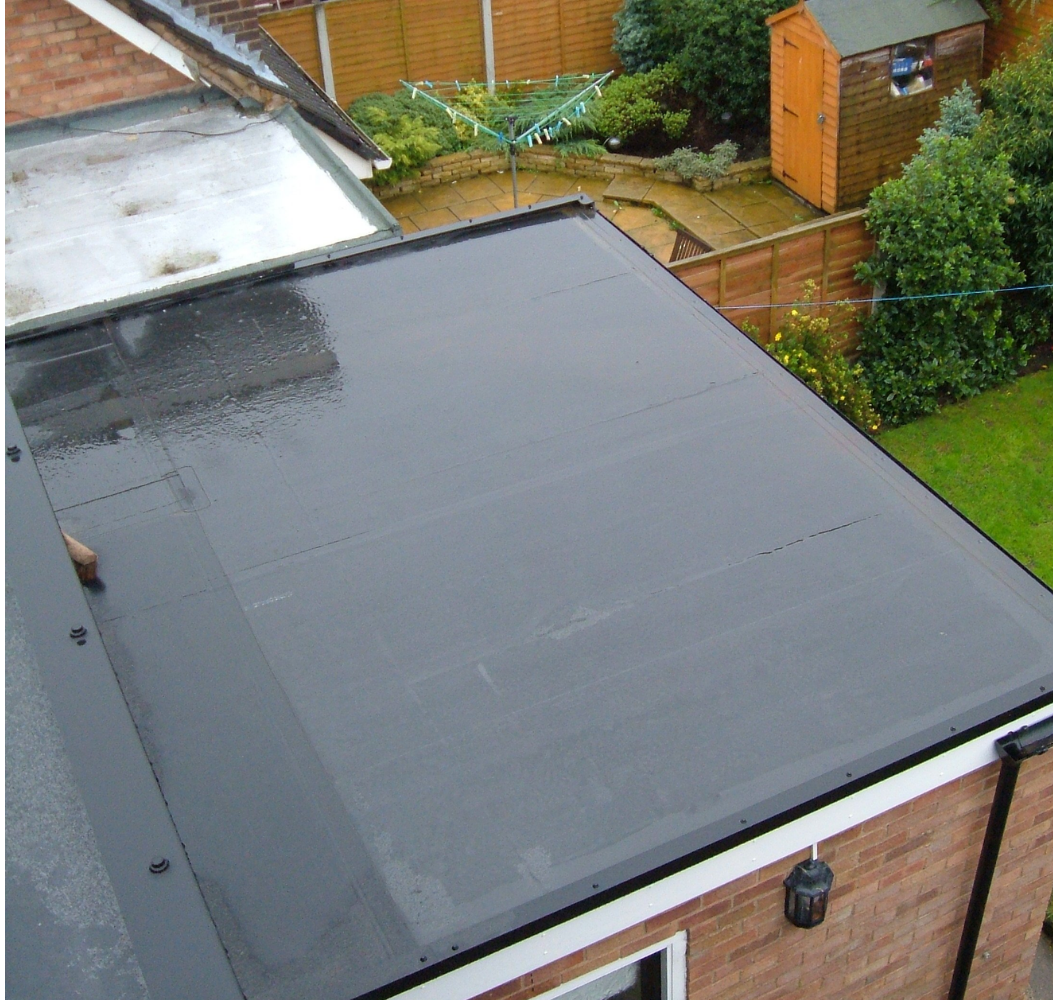 The roof of a house with a black roof and a shed in the background.