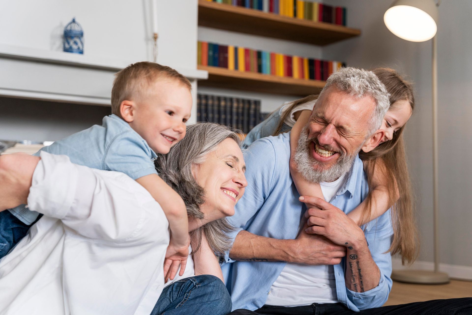 Two children playfully hugging smiling grandparents indoors.