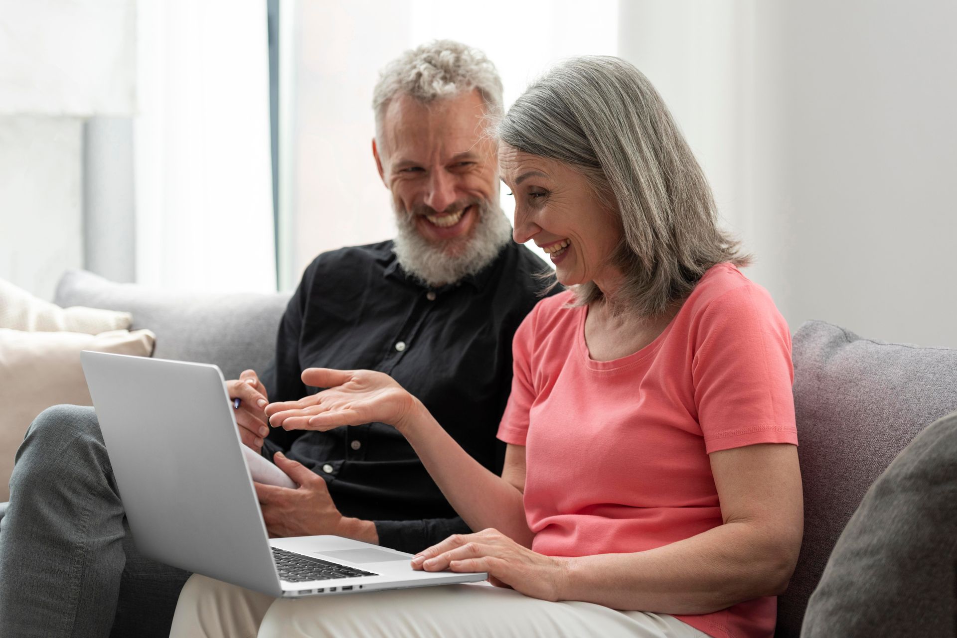 Couple looking at laptop; woman pointing, both smiling, sitting on couch indoors.