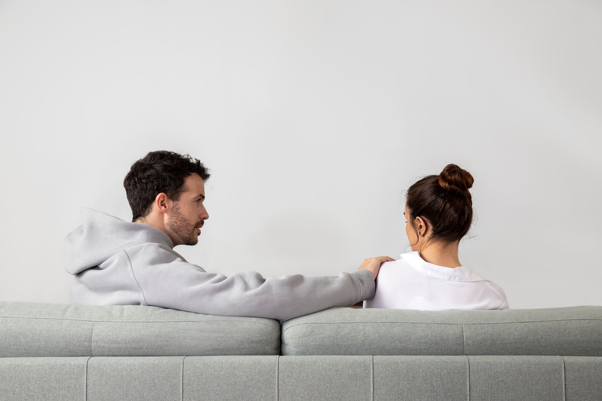 Man in gray hoodie consoles woman in white shirt on a couch.