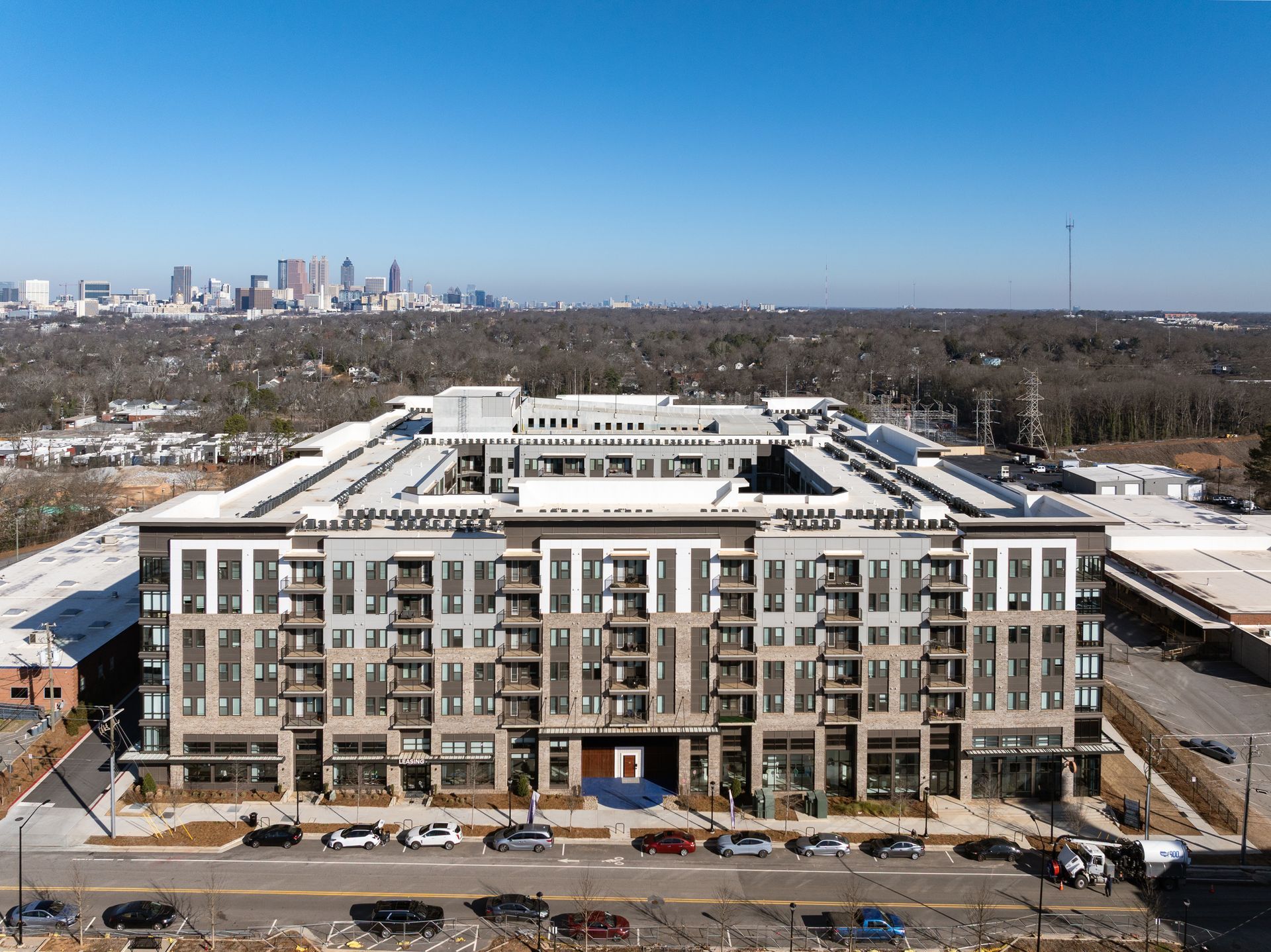 Aerial view of a large modern apartment complex in a suburban setting, with a city skyline visible in the distance.