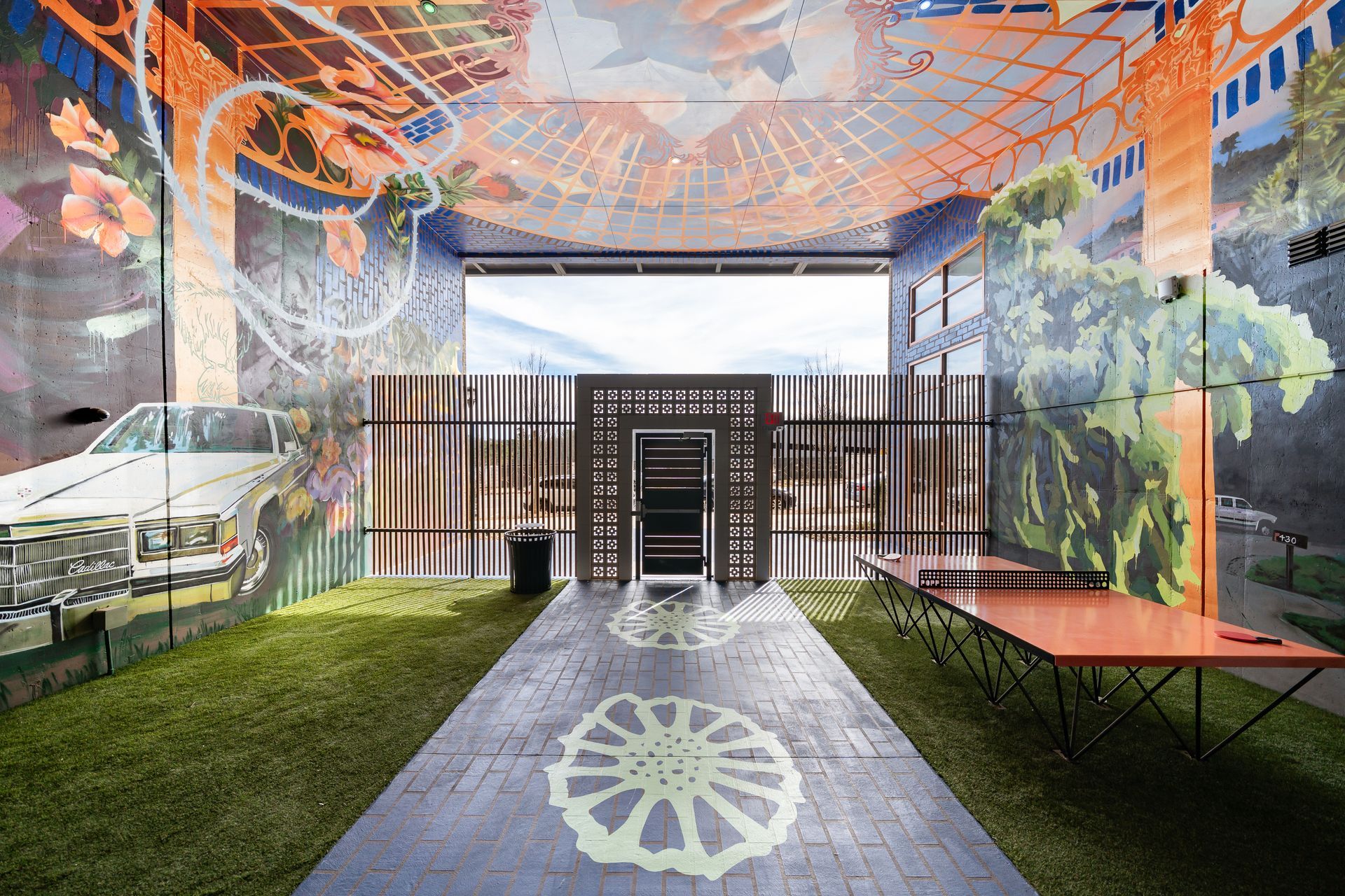 A vibrant, artistic indoor space with a painted mural, a white car, a patterned path, and an orange ping-pong table.