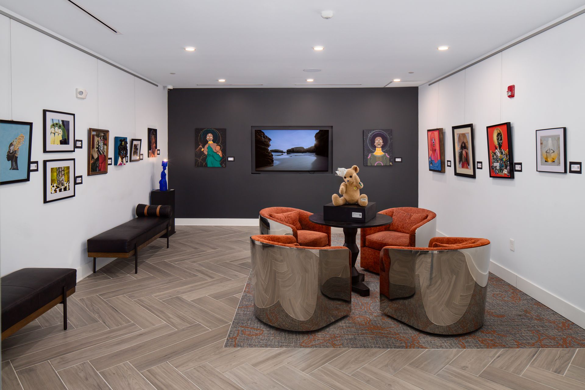 Art gallery interior with a seating area, framed artworks on white walls, and a central display with a small sculpture.