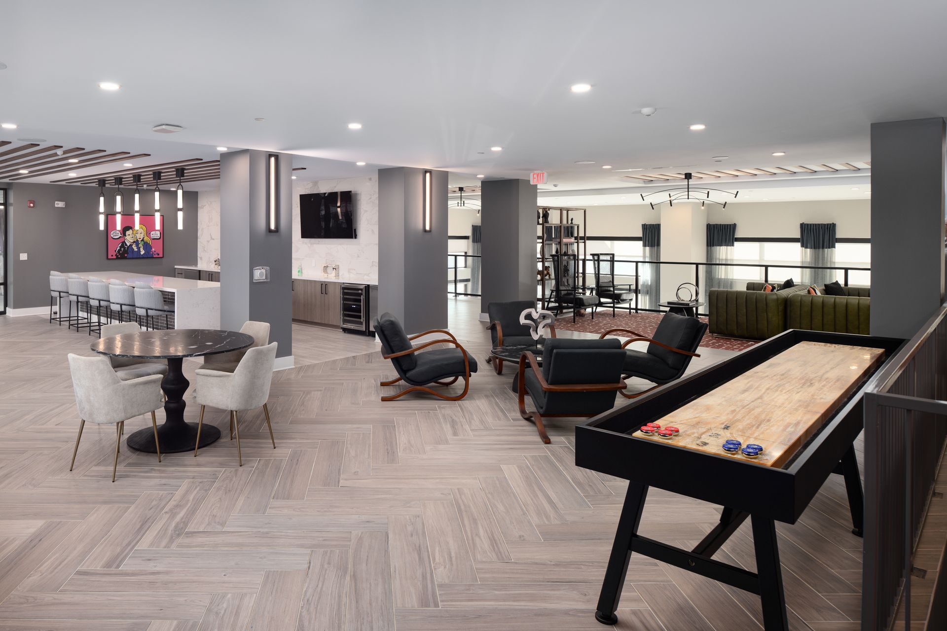 A modern indoor lounge area with a shuffleboard table, seating groups, and a bar counter with stools.