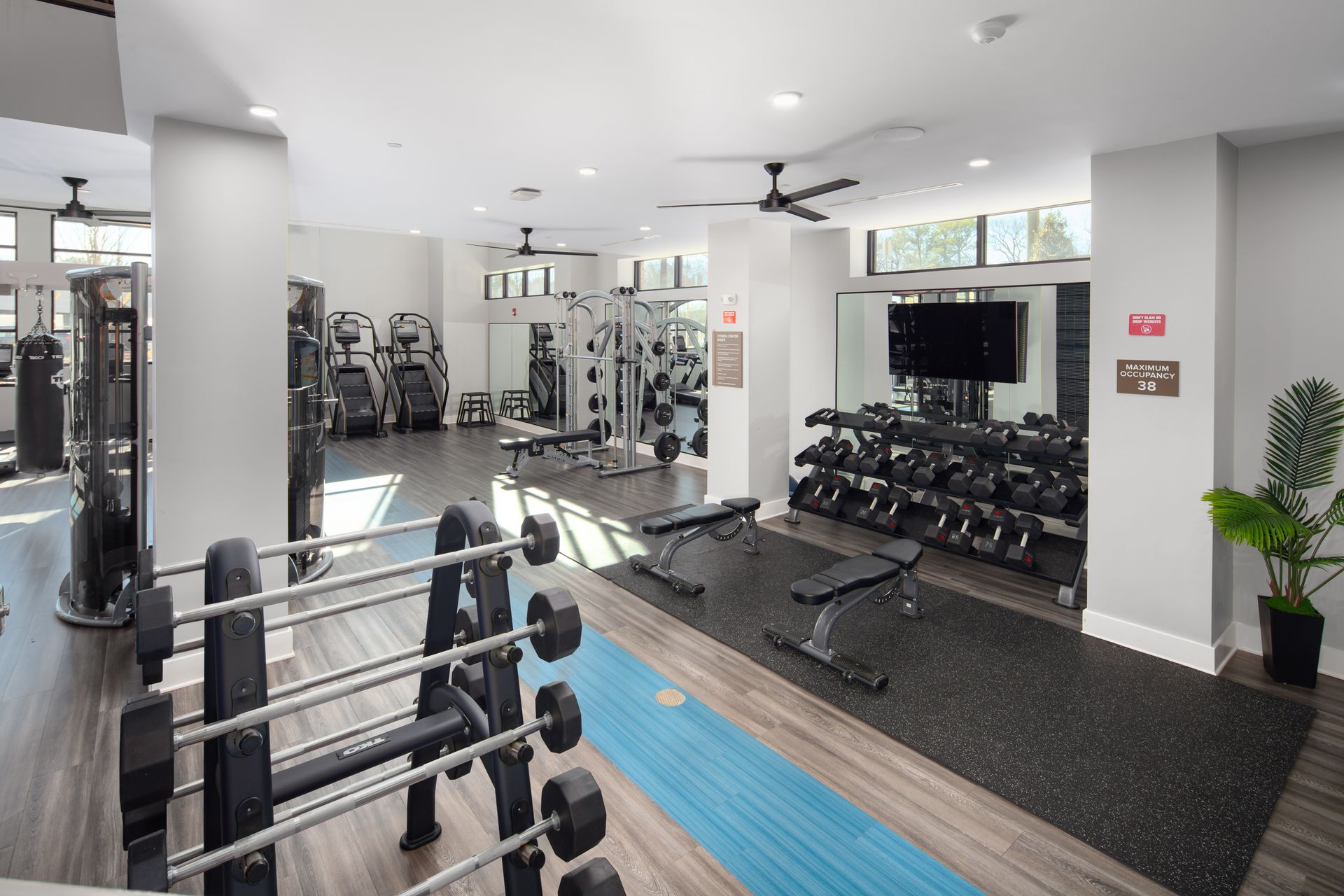 A well-lit, modern gym featuring dumbbell racks, weight benches, strength machines, and a blue workout track.