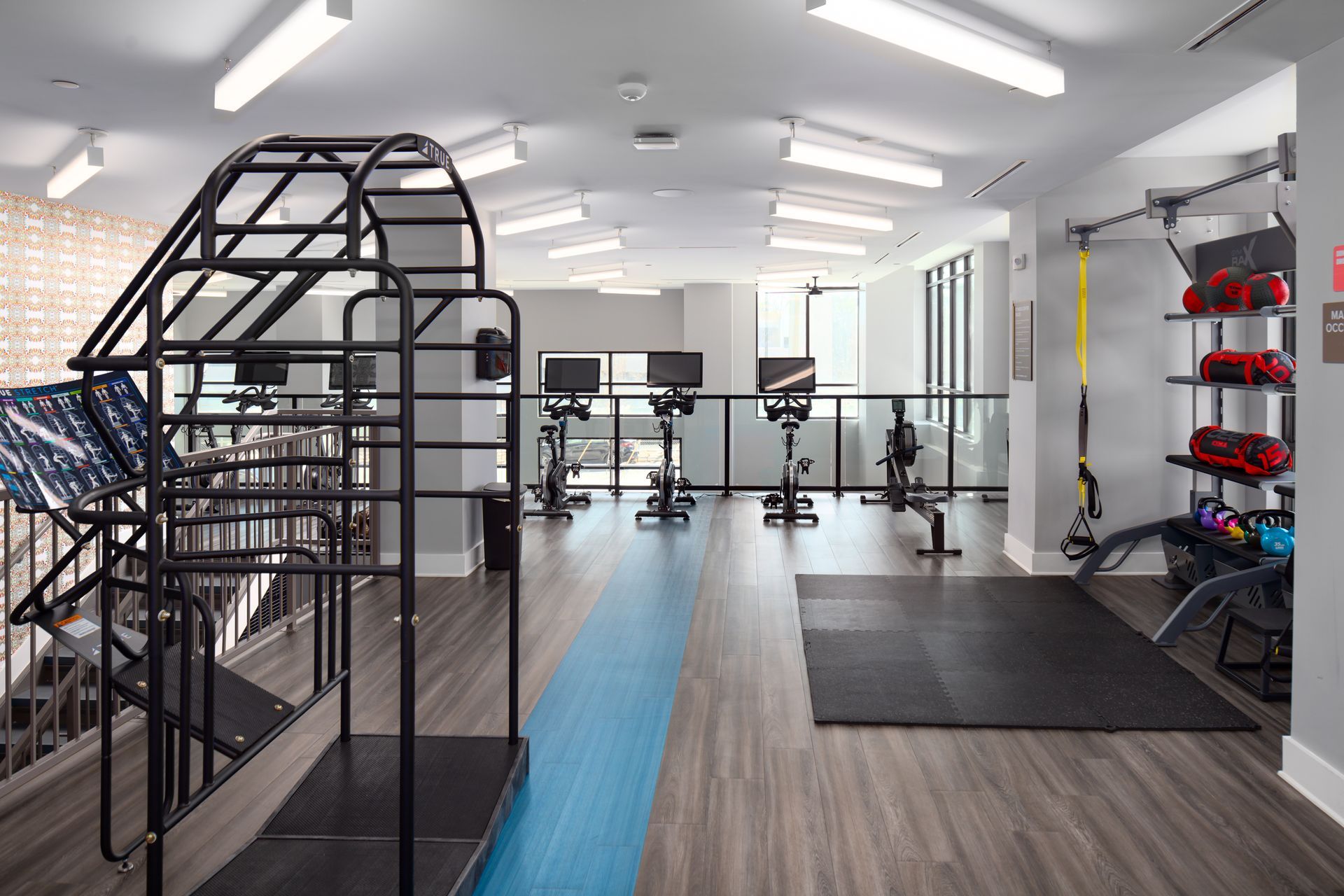 Modern gym interior with a black climbing rig, stationary bikes, a blue track lane, and a weight rack with kettlebells.
