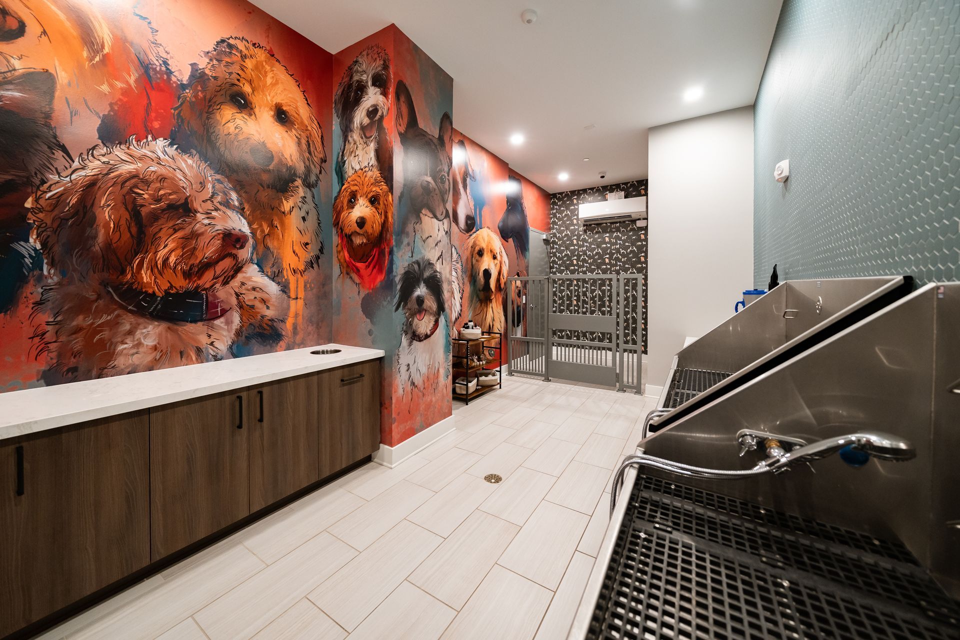 A modern pet wash station with a mural of dogs, a dark cabinet, tiled floors, and a stainless-steel dog wash tub.