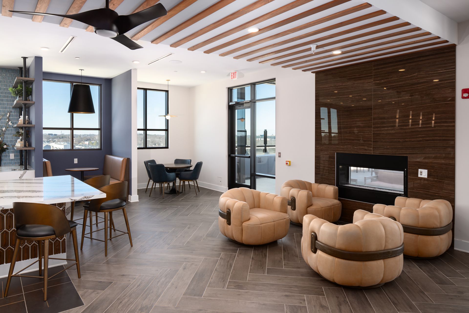 Modern lounge area with a fireplace, beige armchair seating, and wooden slatted ceiling in a brightly lit room.