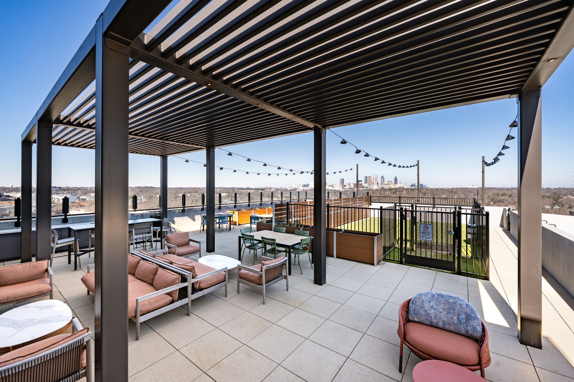 A rooftop terrace with a pergola, string lights, and outdoor seating furniture overlooking a city skyline.
