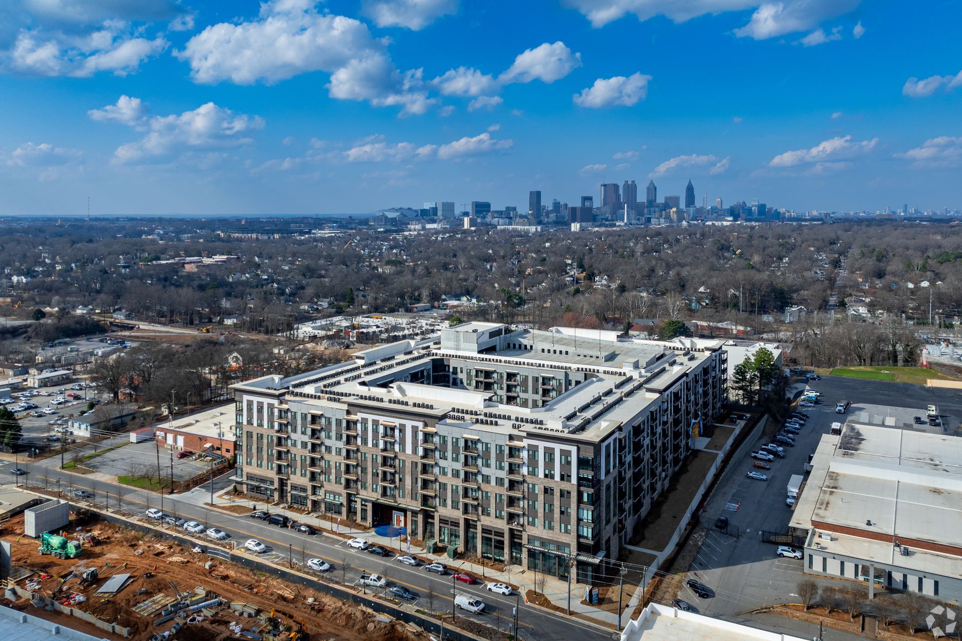 Aerial view of a multi-story apartment complex with a central courtyard, set against a distant city skyline.