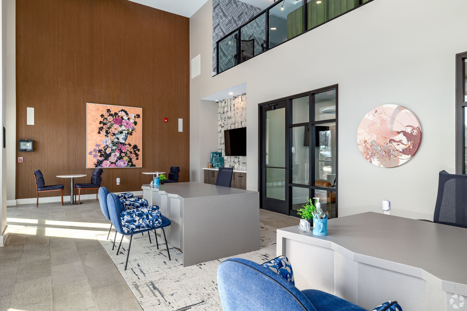 A bright, modern leasing office with desks, blue patterned chairs, a wooden feature wall, and abstract wall art.