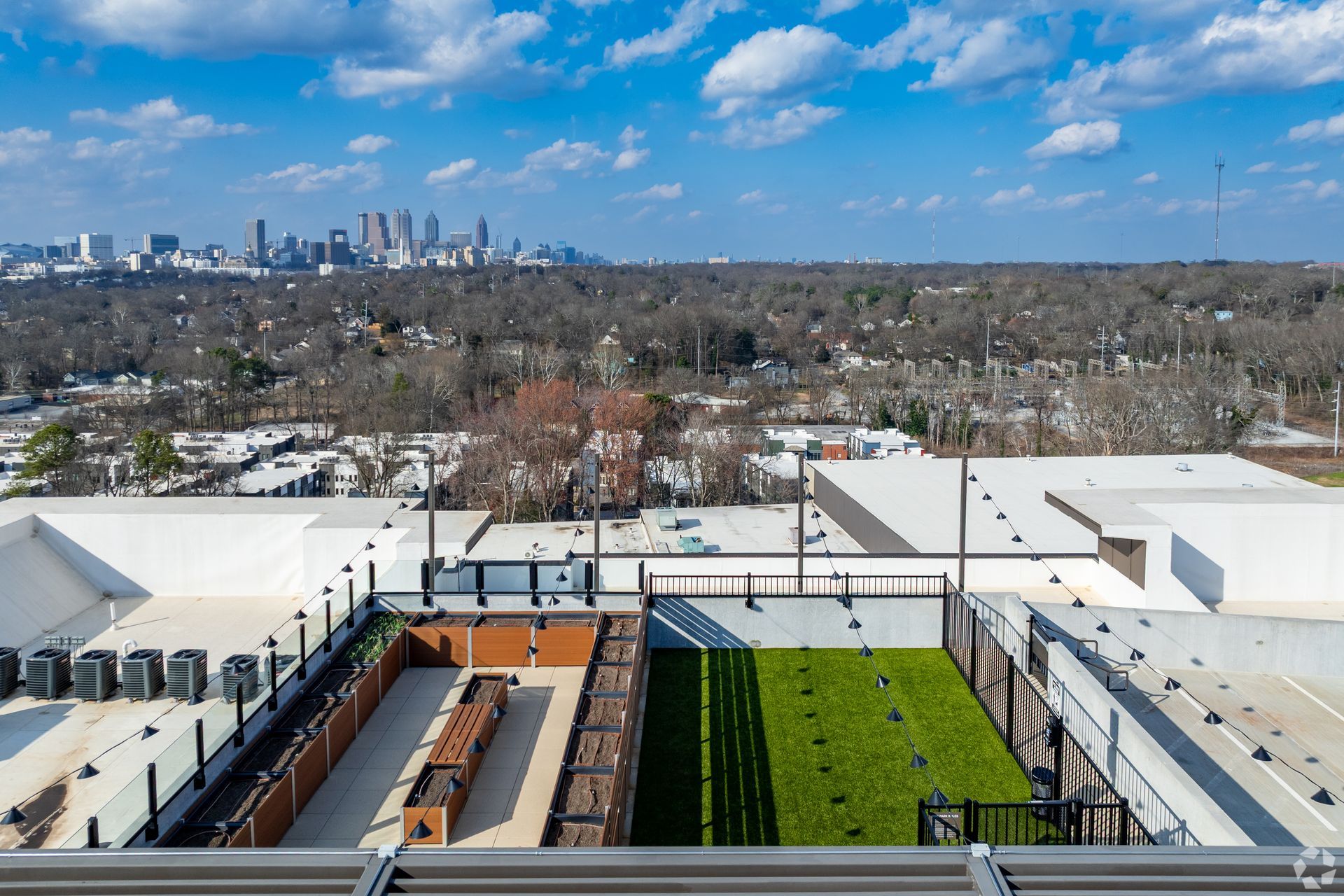 A rooftop terrace with a green lawn and seating area, overlooking a suburban neighborhood and a distant city skyline.