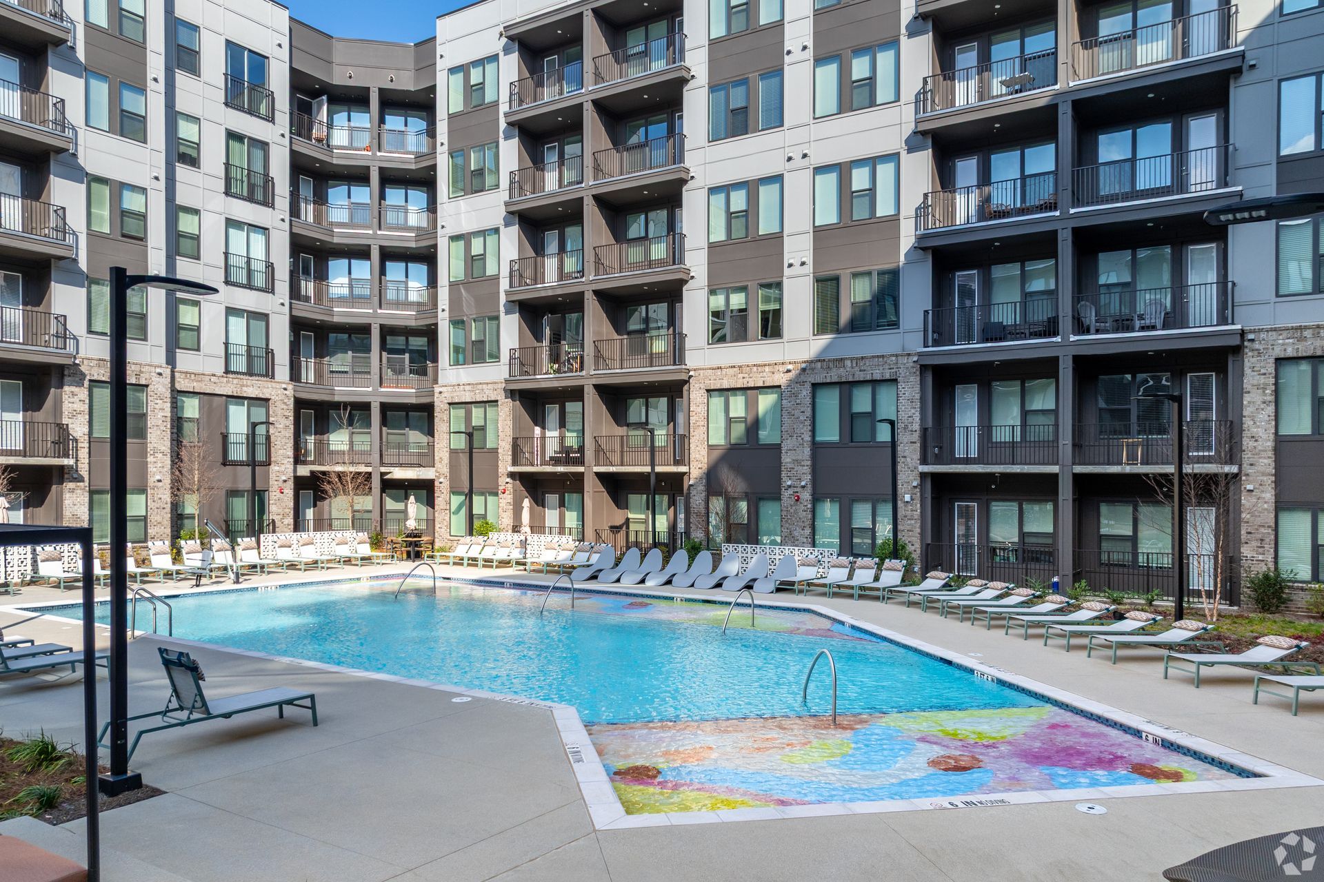 Modern apartment complex with a central outdoor swimming pool and lounge chairs on a sunny day.
