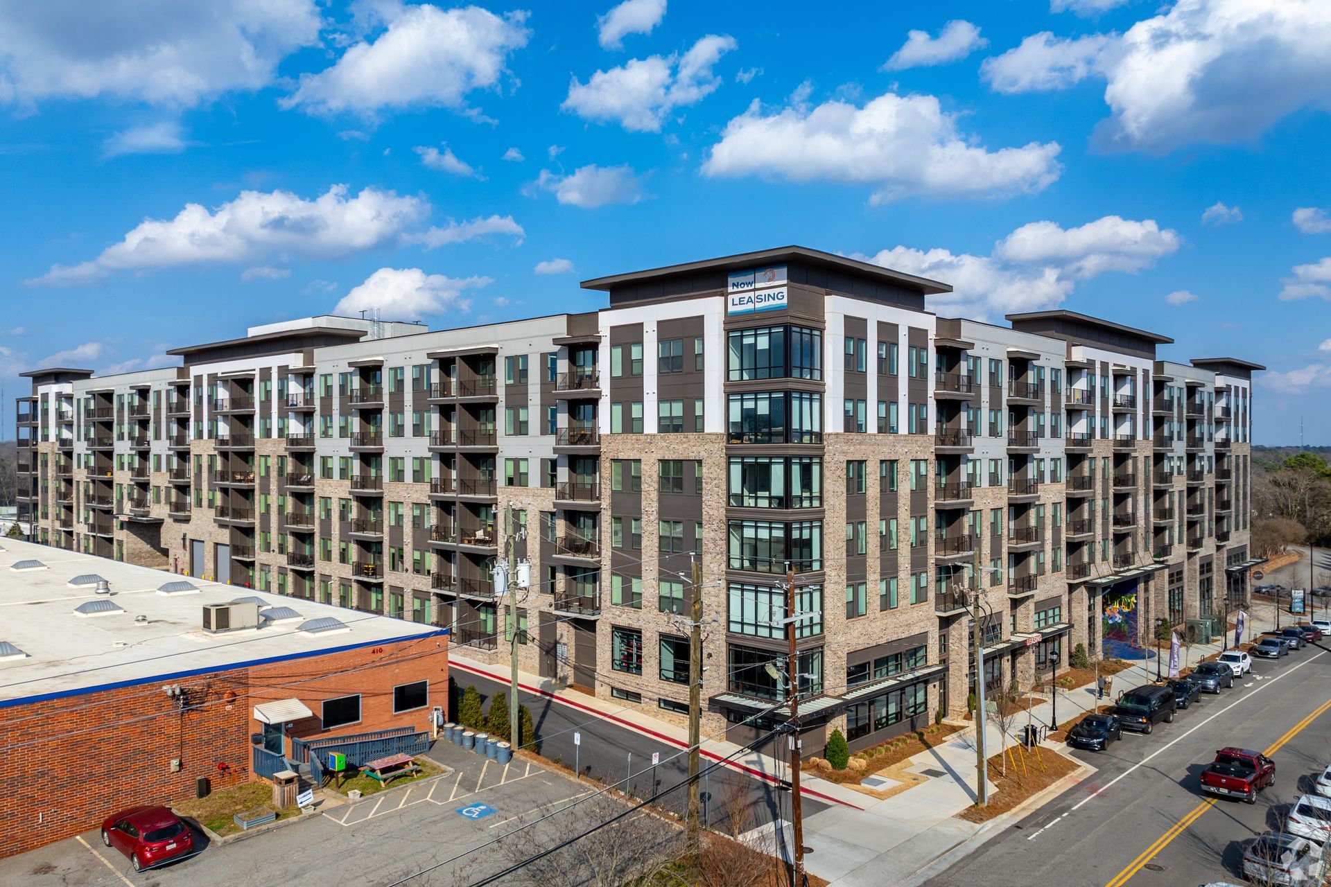 A multi-story apartment building with stone and grey facade, balconies, and an adjacent brick building on a city street.