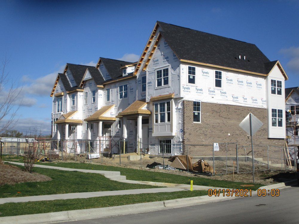 A row of three new townhouse units under construction with unfinished siding, brick bases, and black shingled roofs.