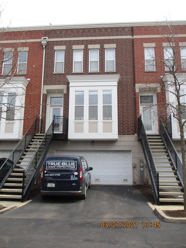 Three-story brick townhouses with metal staircases, a bay window, and a dark van parked in the central garage entrance.