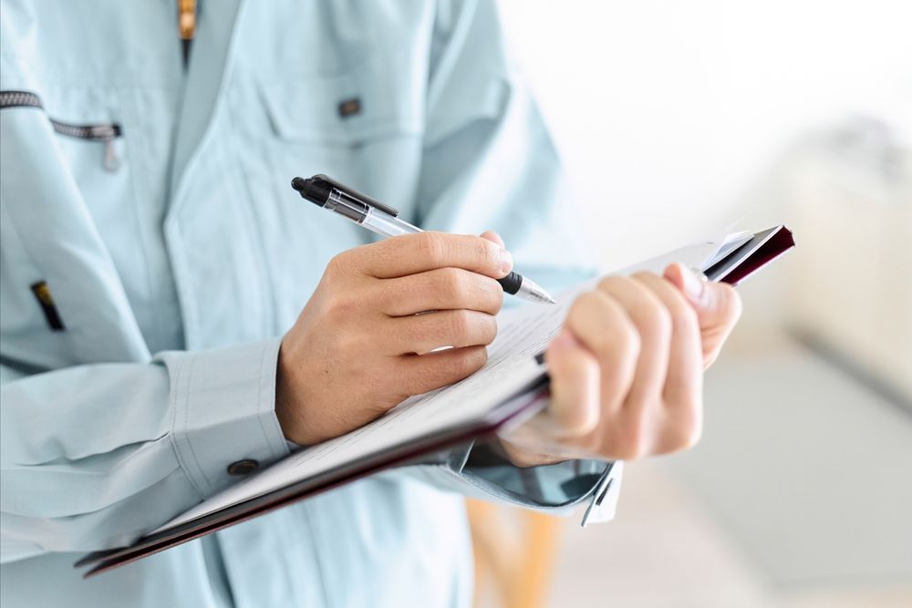 A person in a light blue uniform writing on a clipboard held against their chest.