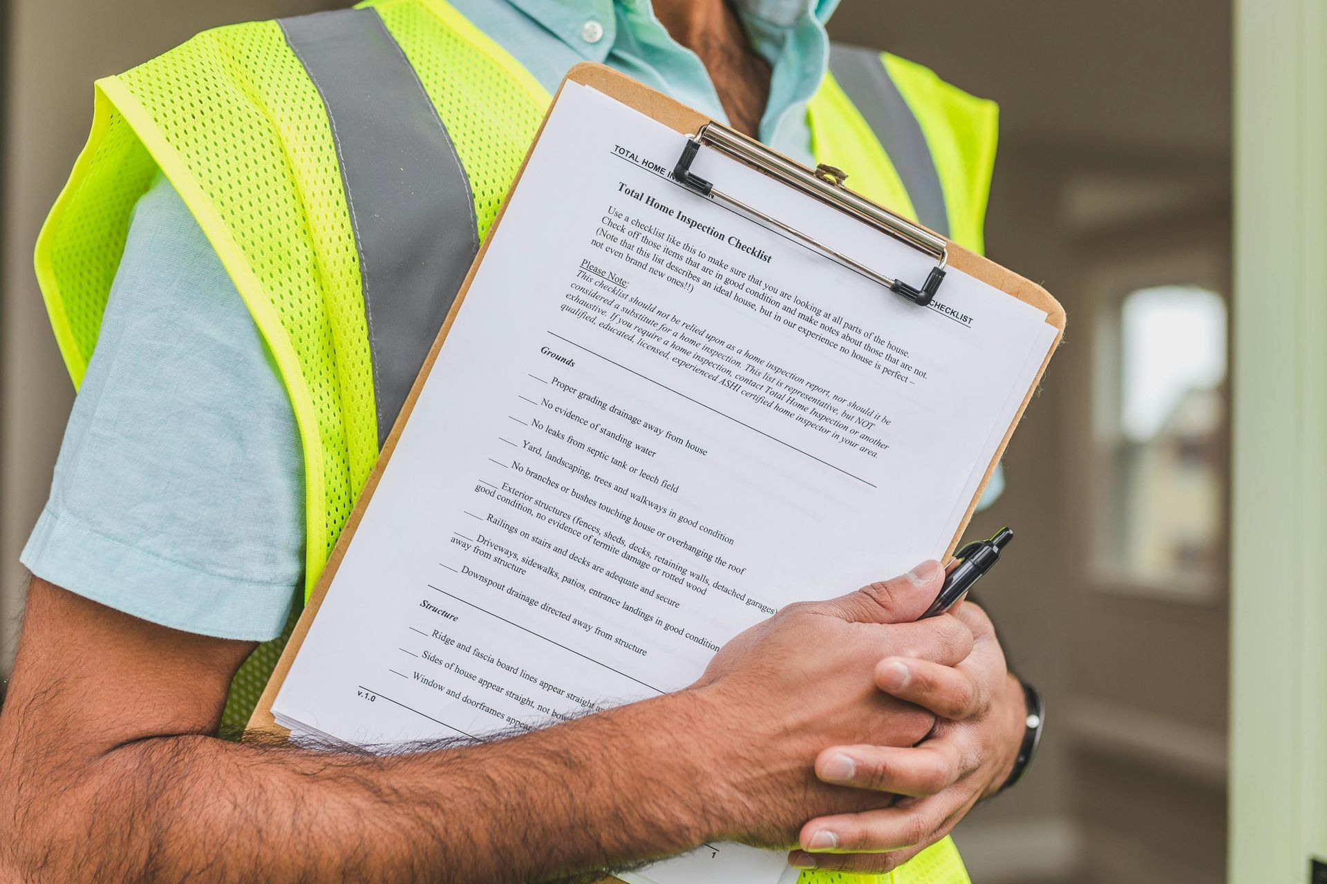 A person in a high-visibility vest holds a clipboard with a checklist while standing in a building.
