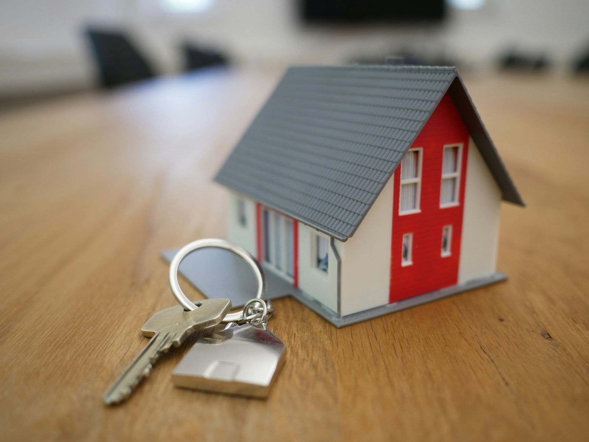 A small house model with a red door and a metal key on a wooden table.