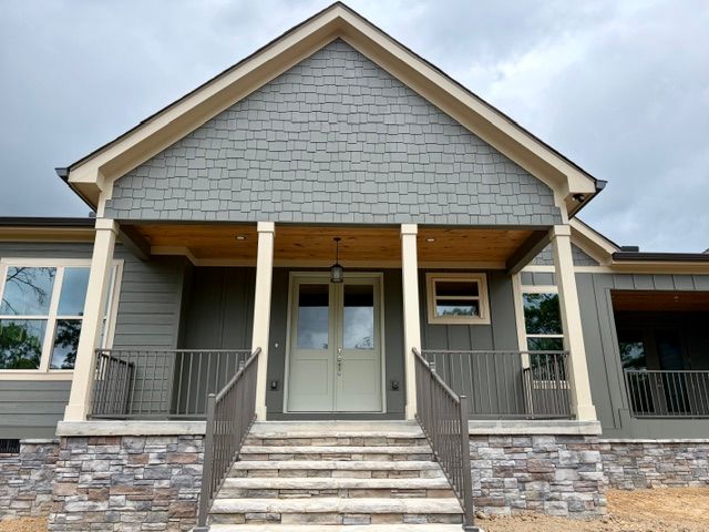Front view of a small house with steps, porch, gray siding, and stone foundation