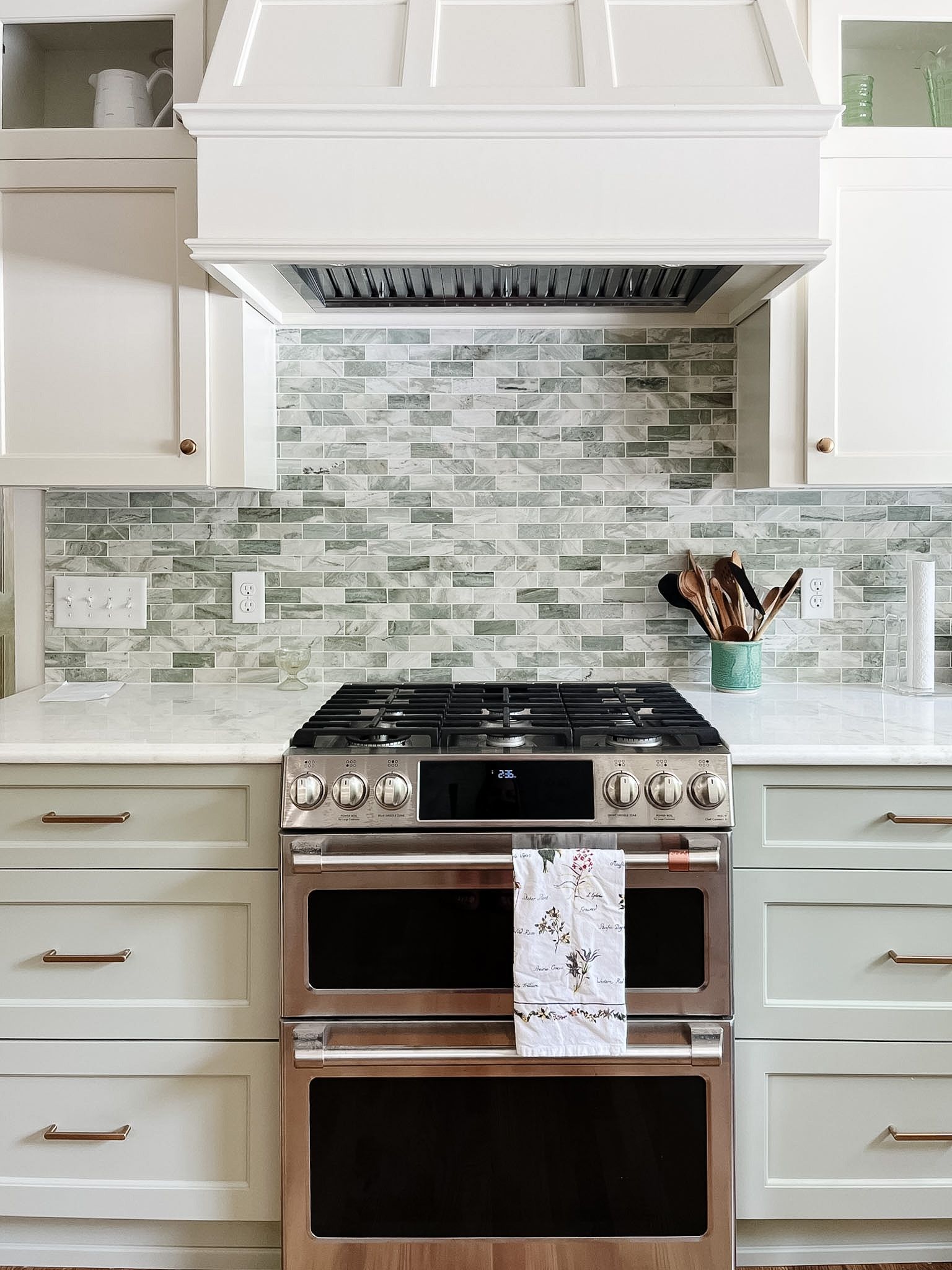 Bright white kitchen with stainless steel stove, hood, and mosaic tile backsplash