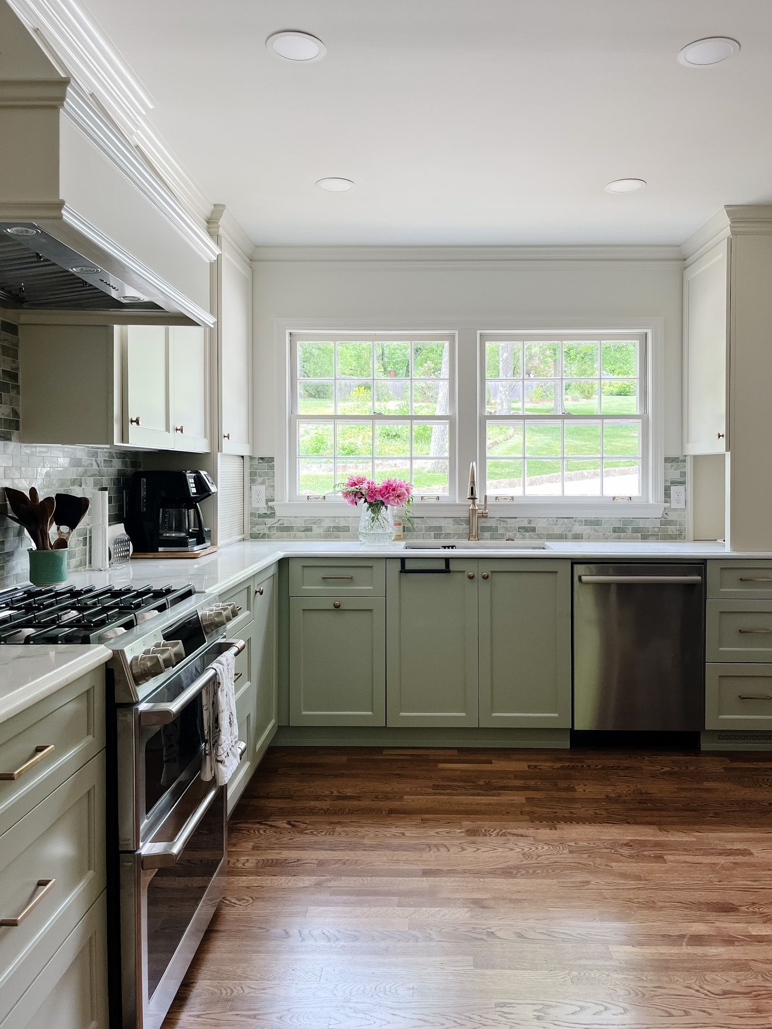 Bright kitchen with white cabinets, green lower cabinets, stainless stove and dishwasher, and a window over the sink.
