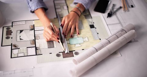 Hands of an architect using a ruler and pencil to work on a colorful floor plan.