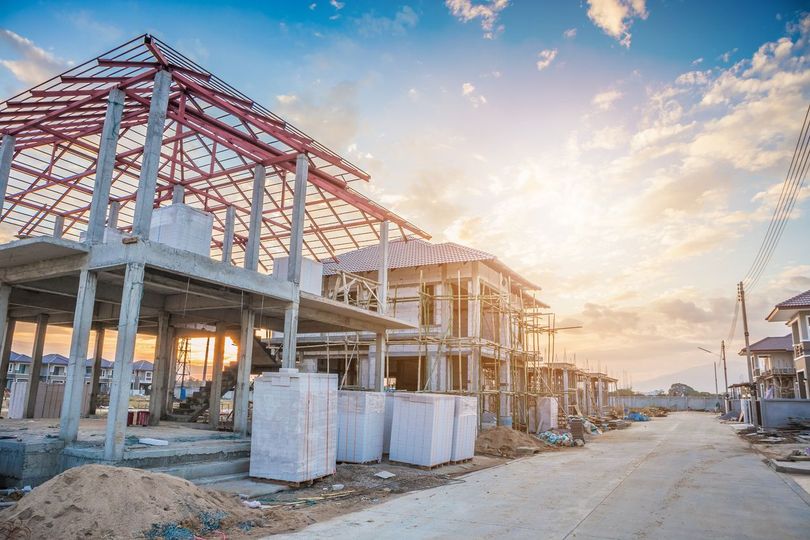 Houses under construction on a sunny street, framing and concrete structures visible.
