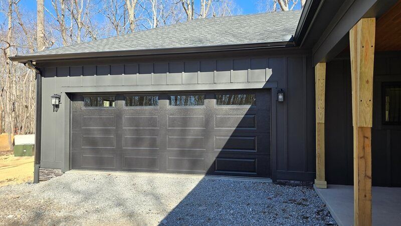 Black garage with a matching door, gravel driveway, and wood trim.