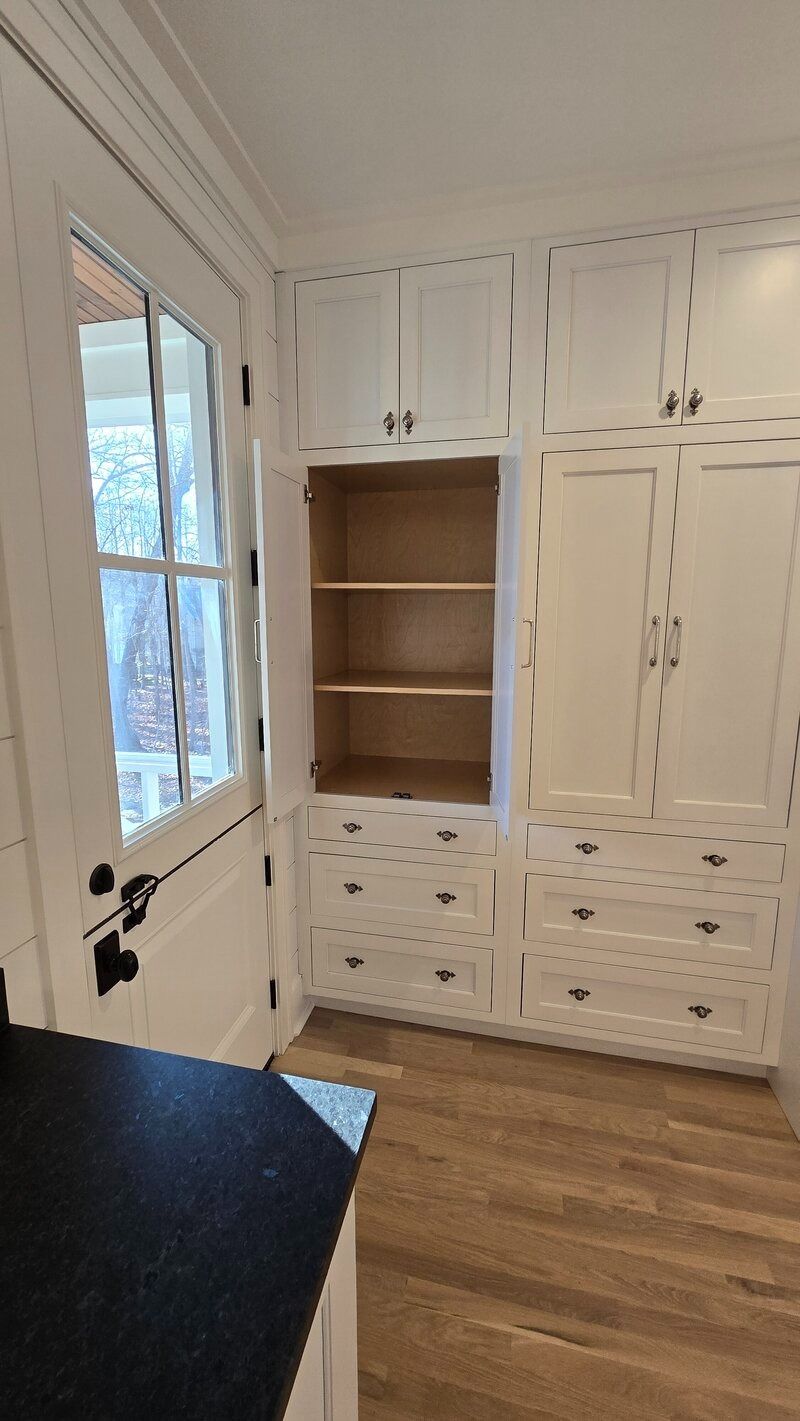 White kitchen cabinets with drawers and a partially open cabinet with wooden shelves next to a white door.