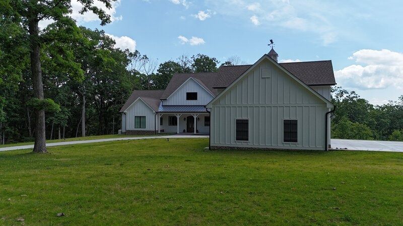 White farmhouse with a green lawn and surrounding trees under a blue sky.
