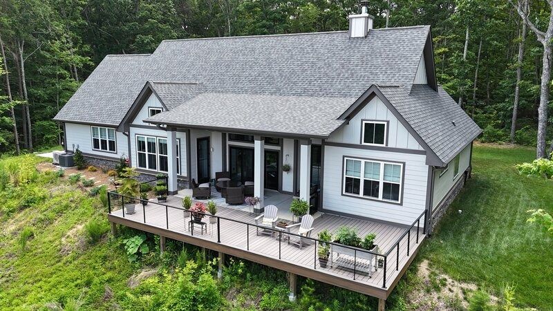 Modern home with gray roof and deck, surrounded by green trees and grass.