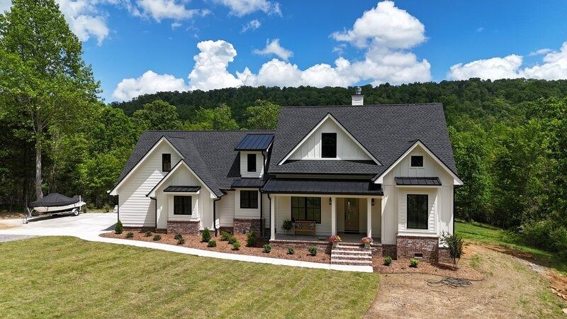White house with black roof and trim, brick accents, surrounded by trees on a sunny day.