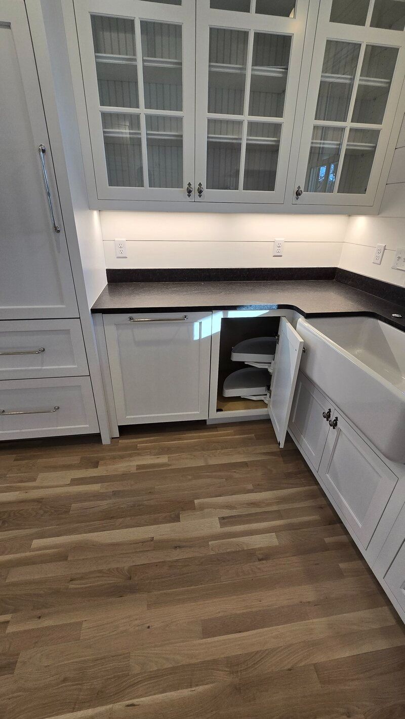White kitchen cabinets, countertop, and pull-out shelves with a farmhouse sink. Wood flooring.