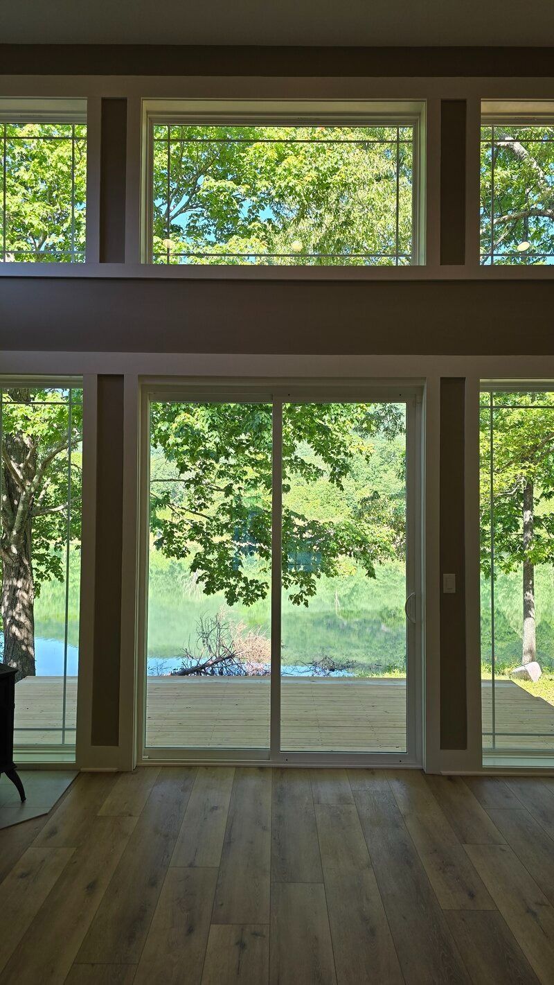 Living room with large windows, sliding door overlooking a wooded area and river.