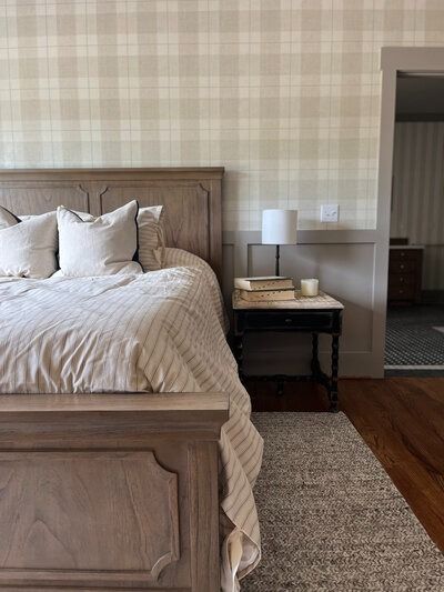 Bedroom with plaid wallpaper, wooden bed, nightstand with lamp, and rug.