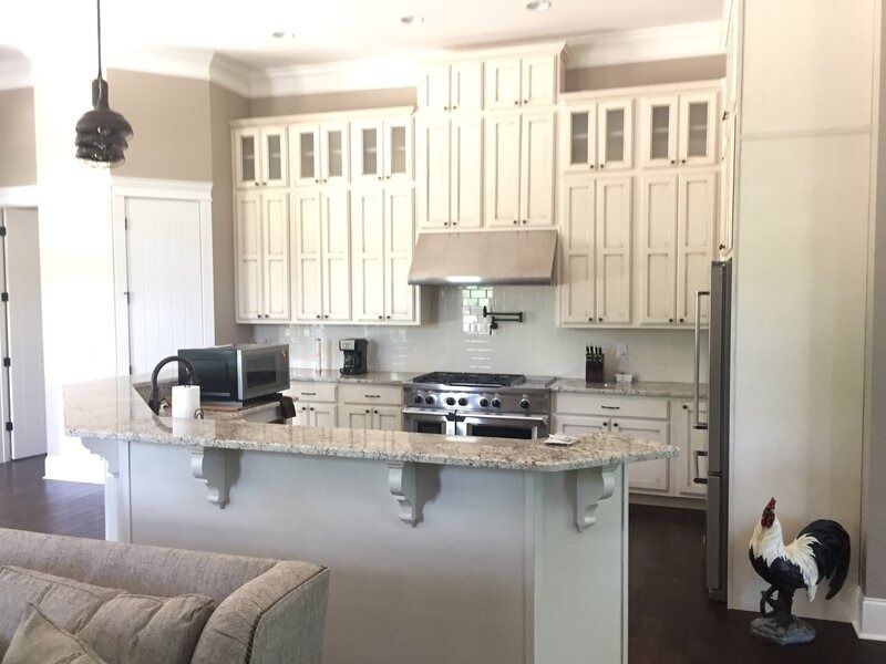 Cream-colored kitchen with island, stainless steel range and hood, granite countertops, and black and white rooster statue.