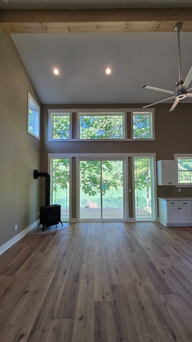 Spacious interior with wood floors, large windows, and a wood-burning stove. Beige walls and a white ceiling.