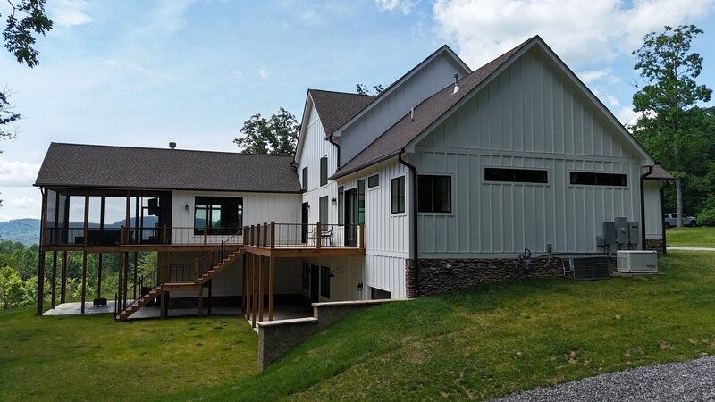 White house with a screened-in porch and deck, set on a grassy hill; brown roof.