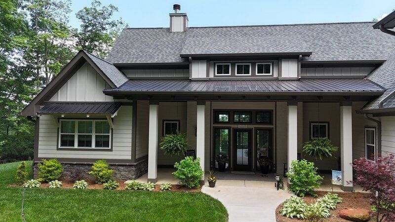 Tan and white house with dark gray roof, front porch, and landscaping.