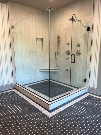 Corner shower with glass doors, tiled walls and floor, and multiple showerheads.