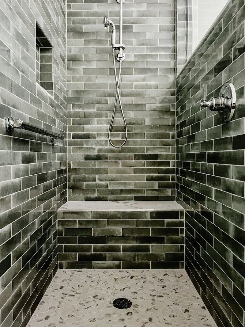 A dark tiled shower with a built-in bench, handheld shower head, and speckled floor.