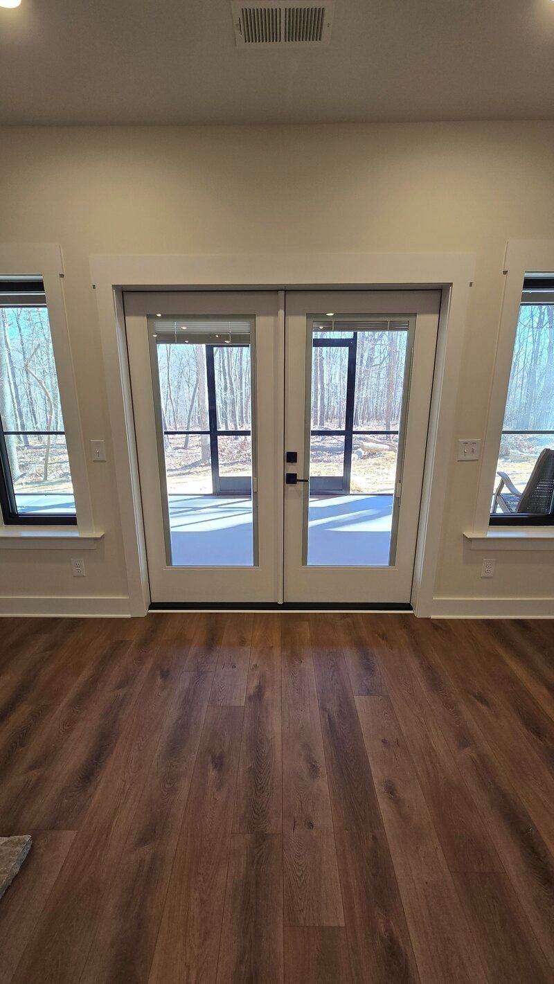 Interior with French doors, two windows. Brown flooring, white trim. Door leads to outside.