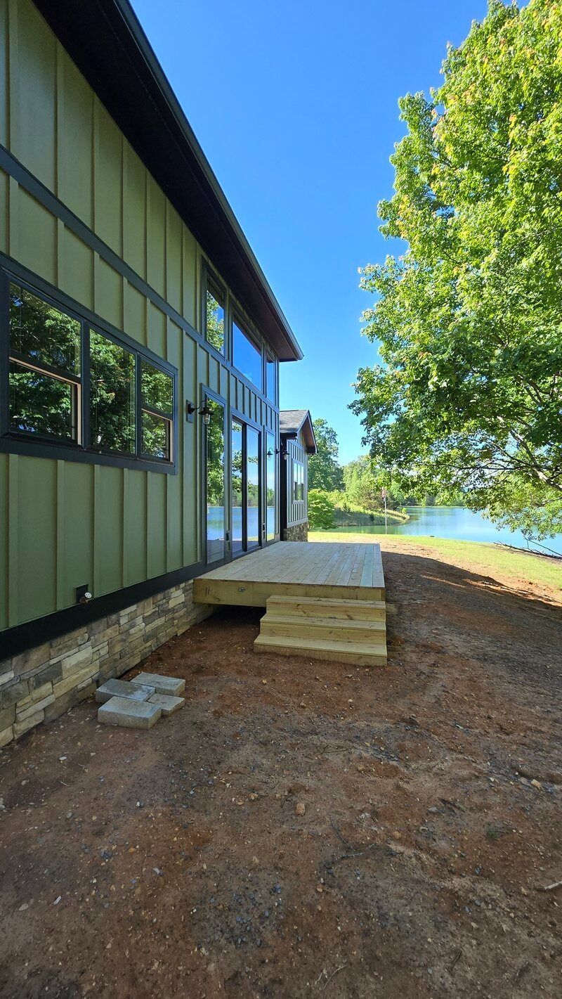 Green house with a deck overlooking a body of water and a tree on a sunny day.