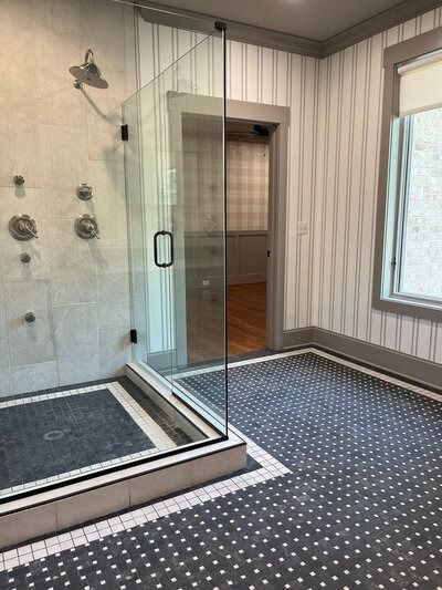 Bathroom with glass shower, patterned floor, striped wallpaper, and window.