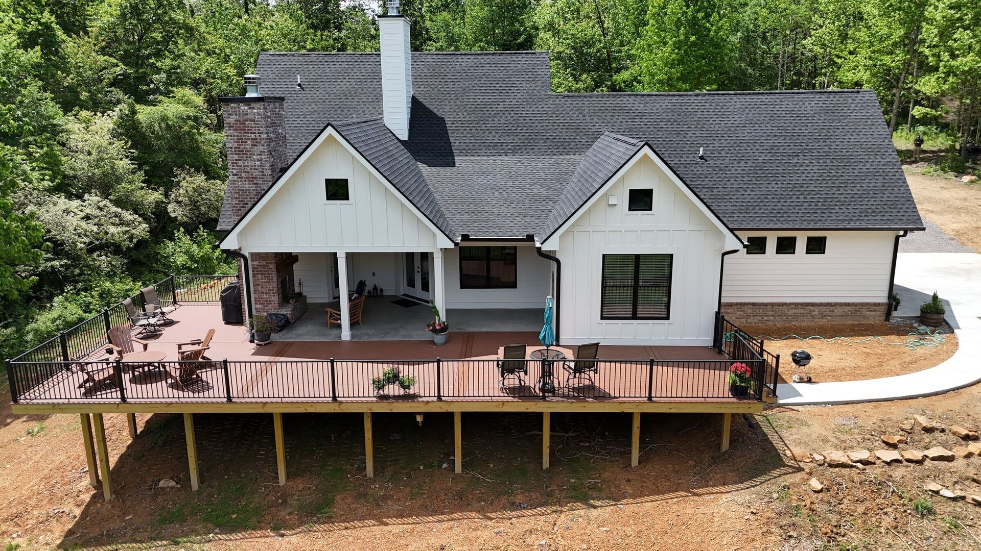White farmhouse with a large deck, surrounded by trees and a circular driveway.
