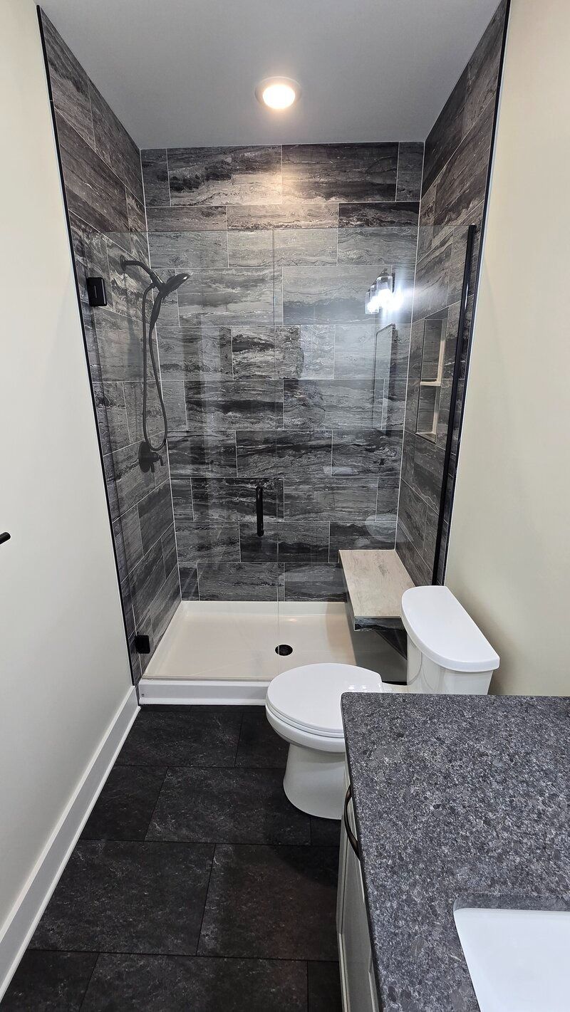 Small bathroom with a walk-in shower, toilet, and vanity. Gray tile shower wall. White and gray tones.